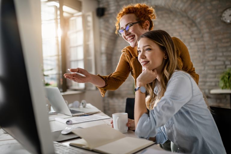 Young happy businesswomen cooperating while using desktop PC in